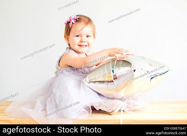 Portrait of a lovely little girl in elegant gray dress in front of a white background. Little princess. Little baby girl playing with silver star-shaped balloon