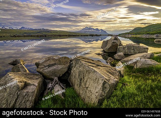 View over Mount Akka reflecting in the water, big rocks in the foreground, in nice evening light in the summer nigh, Stora sjöfallet nationalpark