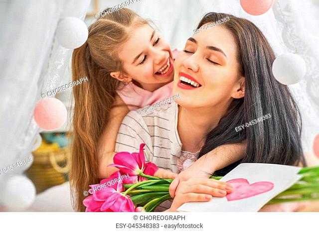 Happy women's day! Child daughter is congratulating mom and giving her flowers tulips. Mum and girl smiling and hugging. Family holiday and togetherness