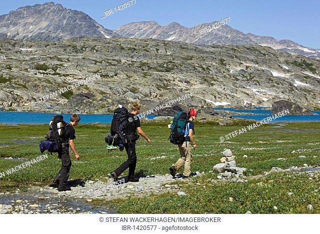 Group of hikers with backpack, hiking historic Chilkoot Pass, Chilkoot Trail, Inuit trail marker, inukshuk, cairn, Crater Lake behind, alpine tundra