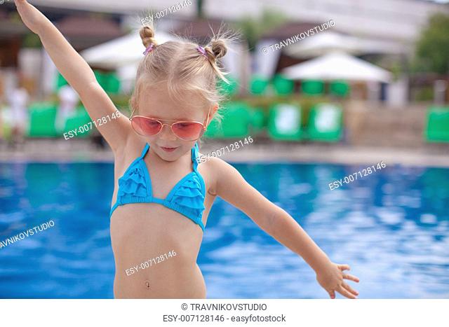 Beautiful little girl spread her arms standing near swimming pool