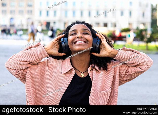 Smiling young with eyes closed listening music through headphones in city