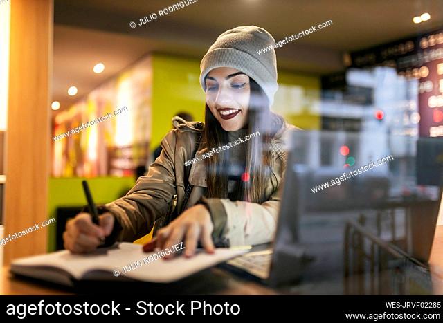Woman writing in diary at cafe seen through glass