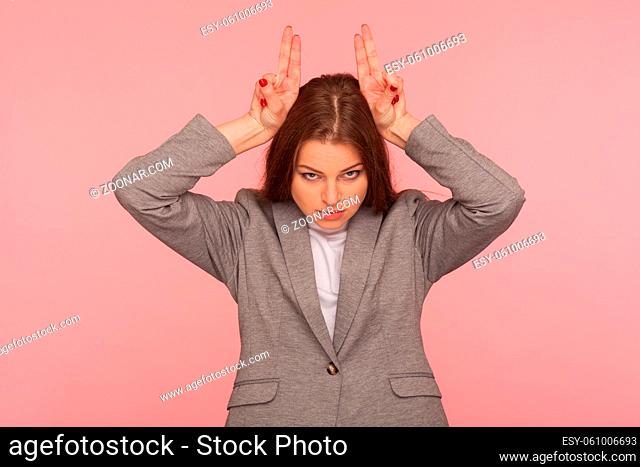 I am dangerous. Portrait of aggressive young woman in business suit standing with bull horn hand sign, antler gesture on head, threatening to attack enemy