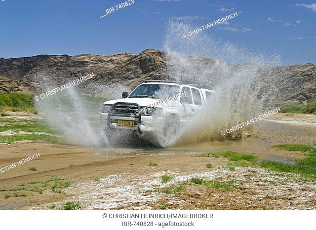 Off-road vehicle (4X4) driving through a large puddle in the otherwise dried-up Huanib River Valley, Kaokoveld, Namibia, Africa