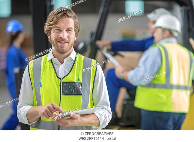 Portrait of smiling man wearing reflective vest holding tablet in factory