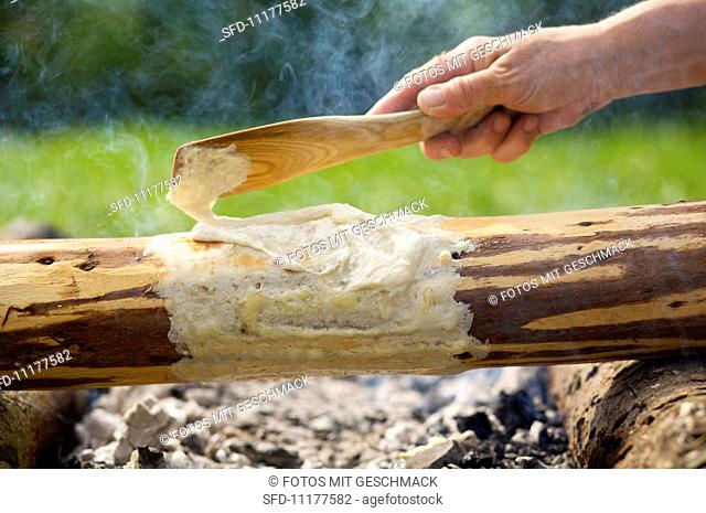 A cake being baked country-style, wrapped around a log over an open fire