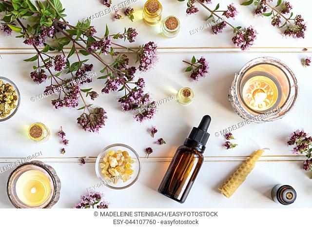 Bottles of essential oil with fresh blooming oregano twigs, frankincense resin and other herbs
