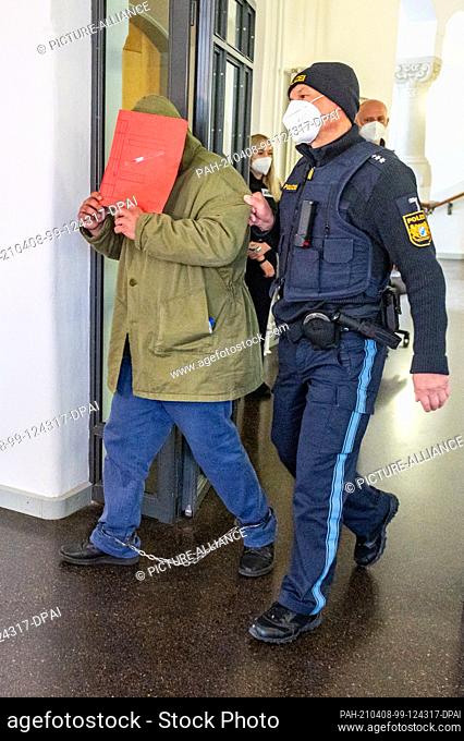 08 April 2021, Bavaria, Regensburg: The defendant is led by a police officer into the hearing room at the regional court
