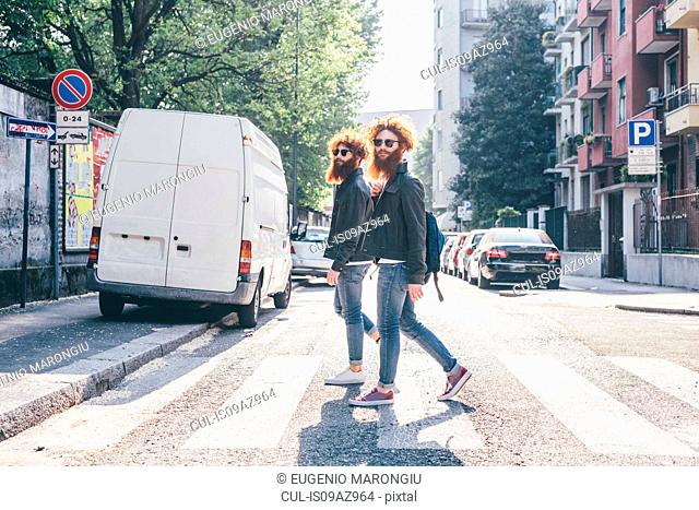 Young male hipster twins with red hair and beards strolling on pedestrian crossing