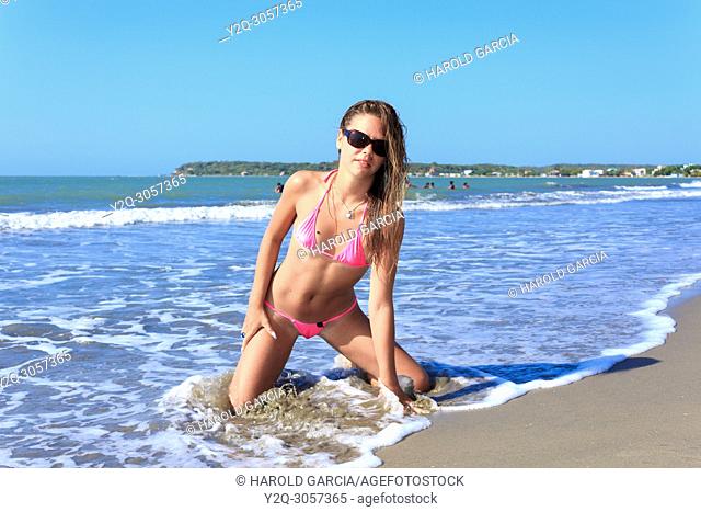Beautiful woman Posing in a super daring swimwear kneeling and getting wet on the beach of Cartagena, Colombia