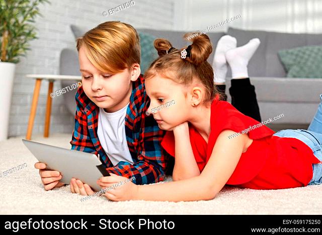cute brother and sister with tablet lying on floor. Children use gadgets at home