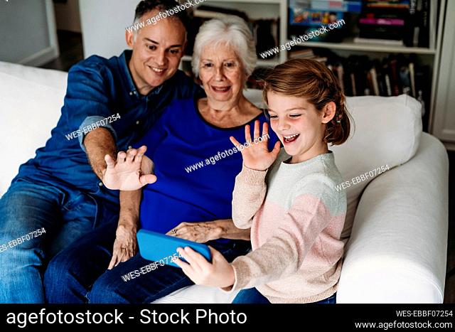 Happy girl with grandmother and father having video call on mobile phone at home