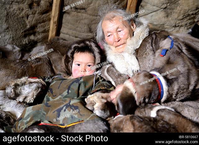 A Nenets older woman with her grandson. Both are dressed in their winter coats, made with reindeer skin and sitting in their tent, Chum, Yar-Sale district