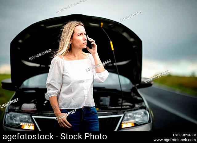 Pretty middle aged woman having car troubles - broken down car on the side of the road, calling the insurance company for assistance