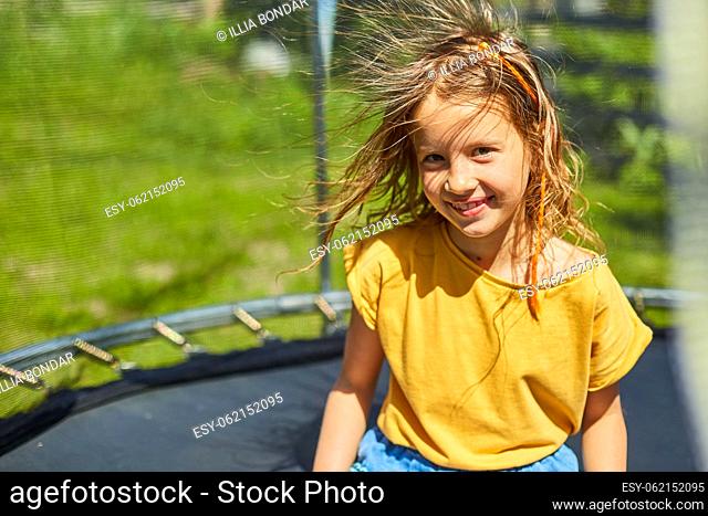 Portrait of young girl with electrified hair on trampoline outdoors, in the backyard of the house on a sunny summer day, summertime vacation