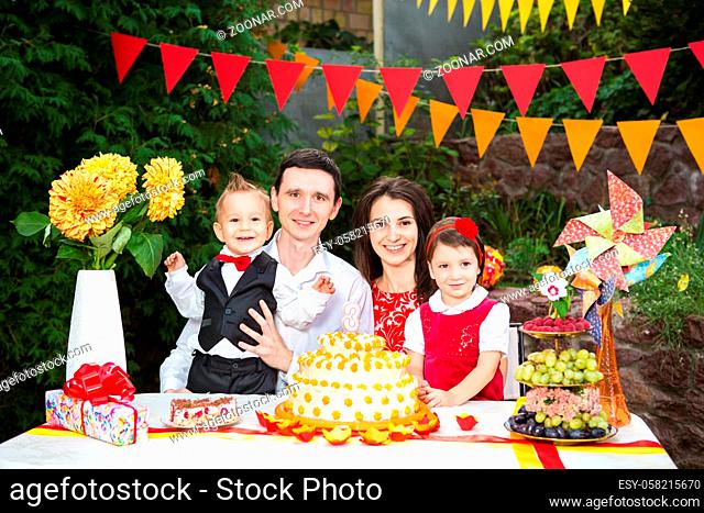 family of four people father mom son and daughter celebrates daughter's birthday three years sitting at a festive decorated table decor and a big delicious cake...