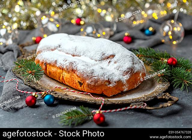 Stollen with raisins, candied fruits, almonds and spices on a metal tray. Traditional Christmas holiday pastry dessert. Background of blurred Christmas lights