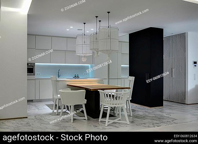 Contemporary kitchen with white walls and gray tiles with patterns on the floor. There is a wooden table with white chairs, kitchen island with a stove
