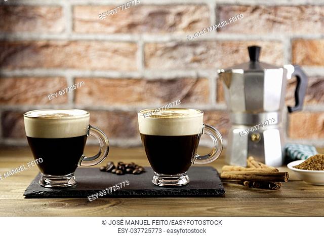 two cup of coffee, Italian coffee maker, coffee beans, cinnamon, napkin and brown sugar bowl on wood table and brick background