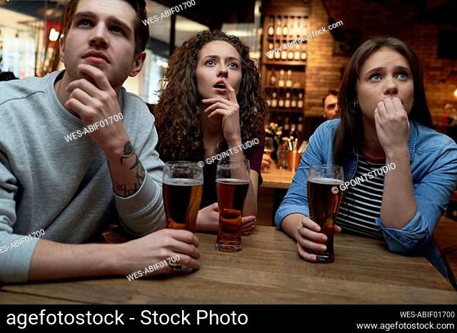 Nervous soccer fans having beer and watching a match together in a pub