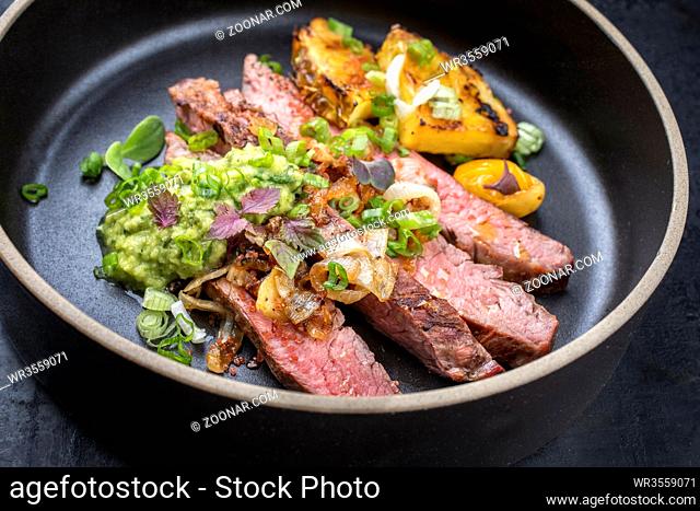 Modern Barbecue dry aged wagyu flank steak with pineapples and chimichurri sauce as closeup on a plate