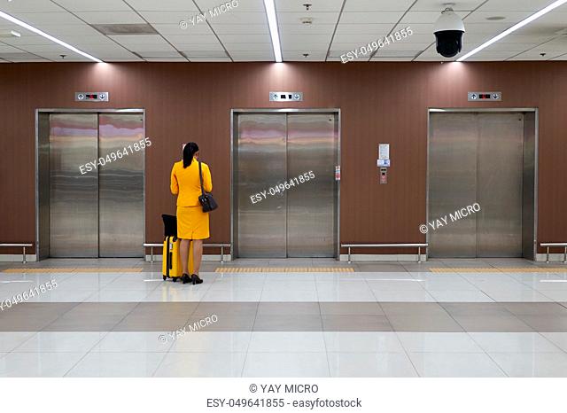 Air hostess with yellow uniform is checking her flight schedule and waiting elevator at the international airport terminal with copy space