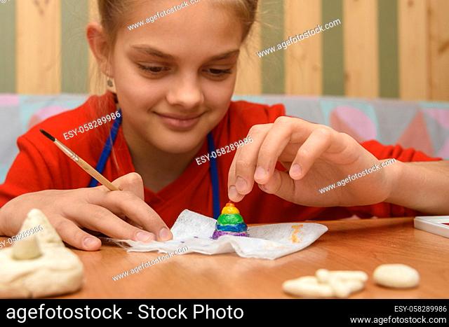 Girl rejoices painting a figurine made of salt dough