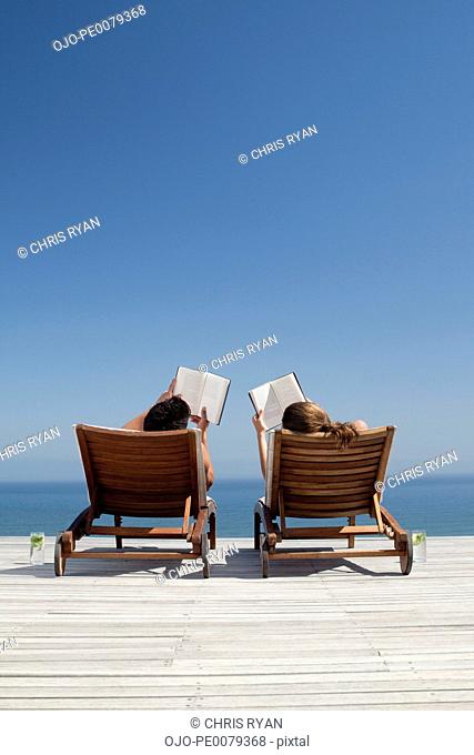 Couple laying in lounge chairs reading books