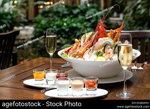 Bowl of gourmet fresh seafood on ice with savory sauce serve with white wine glass on vintage wooden table. Restaurant gastronomy food and drink consumerism...