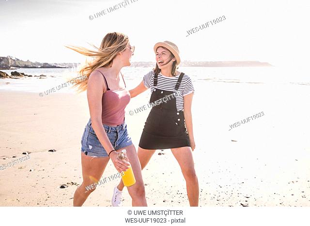 Two girlfriends having fun, running and jumping on the beach