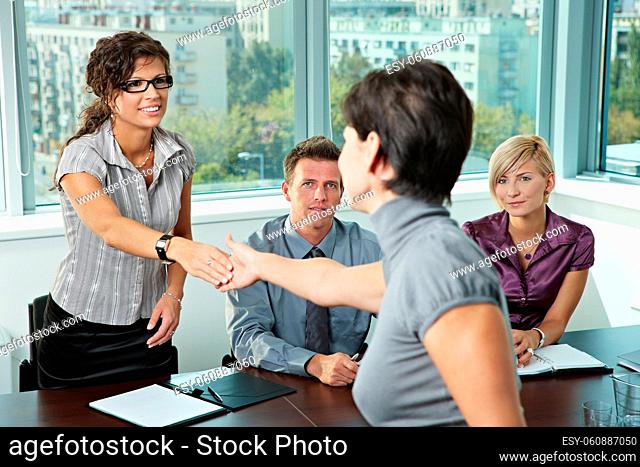 Panel of business people sitting at table in meeting room conducting job interview greeting female applicant