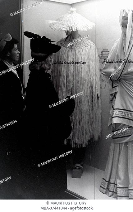 Visitors to a fair in front of a display case with Chinese and Greek costumes, on the occasion of the Wiener Modewoche in the house of fashion Palais Lobkowitz