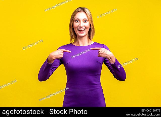 Portrait of joyous winner, excited businesswoman in elegant purple dress smiling broadly and pointing at herself, boasting of achievements