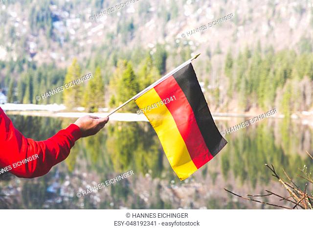 male hiker with red sweater is holding a german flag in the mountains in spring