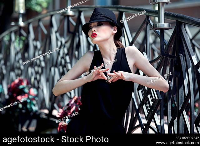 Stylish asian girl in a black suit and hat, posing on metallic bridge