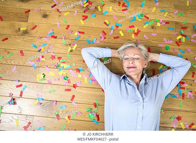 Portrait of smiling senior woman lying on floor covered with confetti