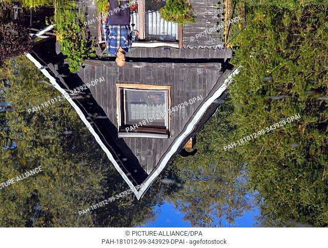 12 October 2018, Brandenburg, Luebbenau: A wooden house on the bank of a river reflected in the water. Photo: Patrick Pleul/dpa-Zentralbild/dpa