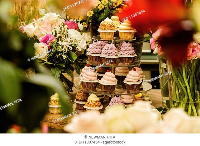 Various cupcakes on a cake stand surrounded by flowers