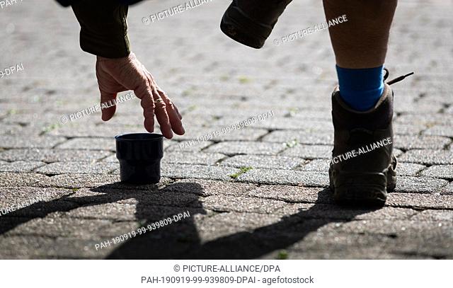 18 September 2019, Lower Saxony, Bad Bentheim: A tourist and hiker reaches for a cup with a hot drink under a bench. The town of Lower Saxony in the county of...