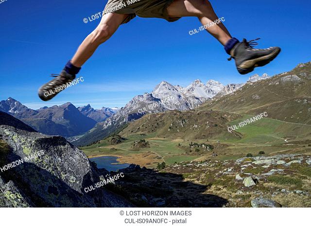 Legs of male hiker jumping over rocks, Lai da Fons, Canton Graubunden, Switzerland