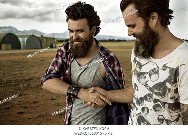 Two men with full beards in abandoned landscape shaking hands