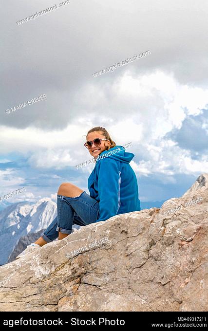 Young woman is sitting on rock, Zugspitzplatt, Zugspitze, Garmisch-Partenkirchen, Wetterstein mountains, Alps, Upper Bavaria, Bavaria, Germany, Europe