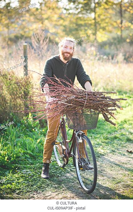 Young man carrying bunch of sticks on bicycle