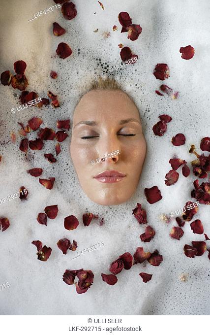 Young woman enjoying foam bath with rose petals