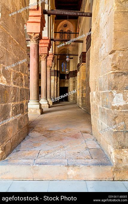 Passage at Sultan Qalawun Mosque with stone columns, colored stained glass windows and wooden door, Cairo, Egypt