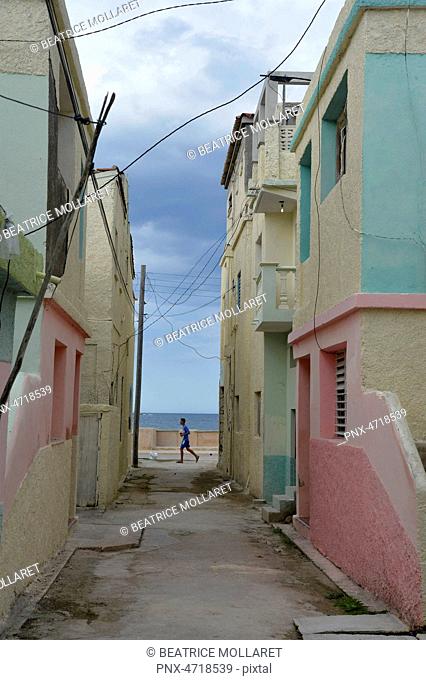 Cuba, Gibara, a young man passes running at the end of a colorful houses