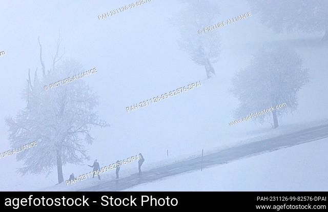 26 November 2023, Baden-Württemberg, Oberried: People stand on a road in the fog near the summit of the Schauinsland. Snowfall lures many people in the...