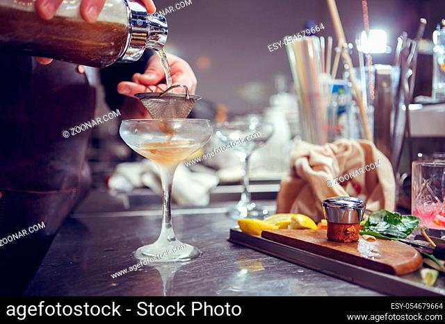 Bartender coocks cocktail behind a bar counter. Toned image
