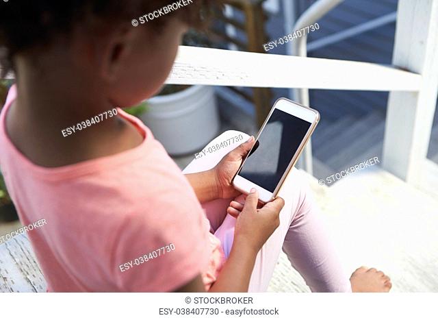 Young Girl Sits On Outdoor Steps Playing With Mobile Phone